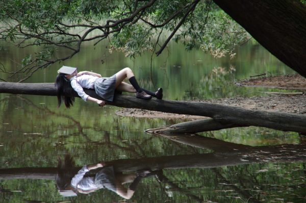 femme allongée sur branche avec livre sur la tête