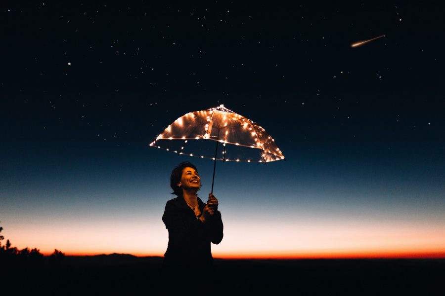 femme devant coucher de soleil riant et tennant un parapluie éclairé